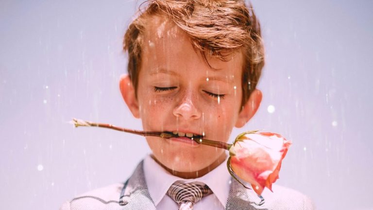 Garoto de olhos fechados com rosa na boca