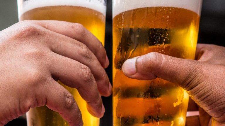 Duas mãos seguram copos de cerveja durante brinde