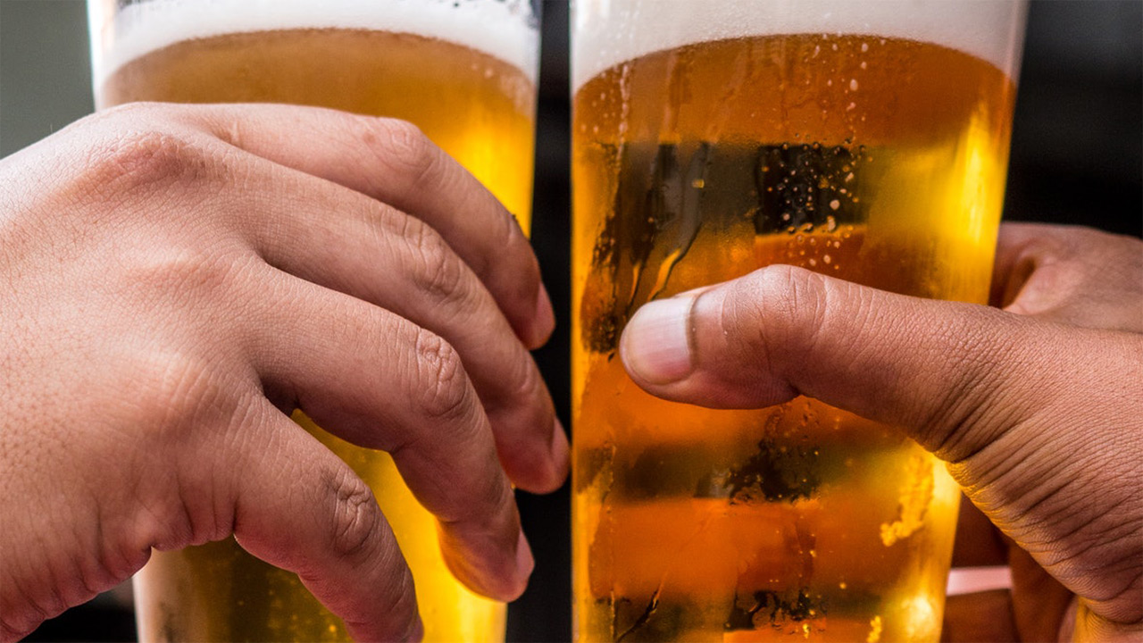 Duas mãos seguram copos de cerveja durante brinde